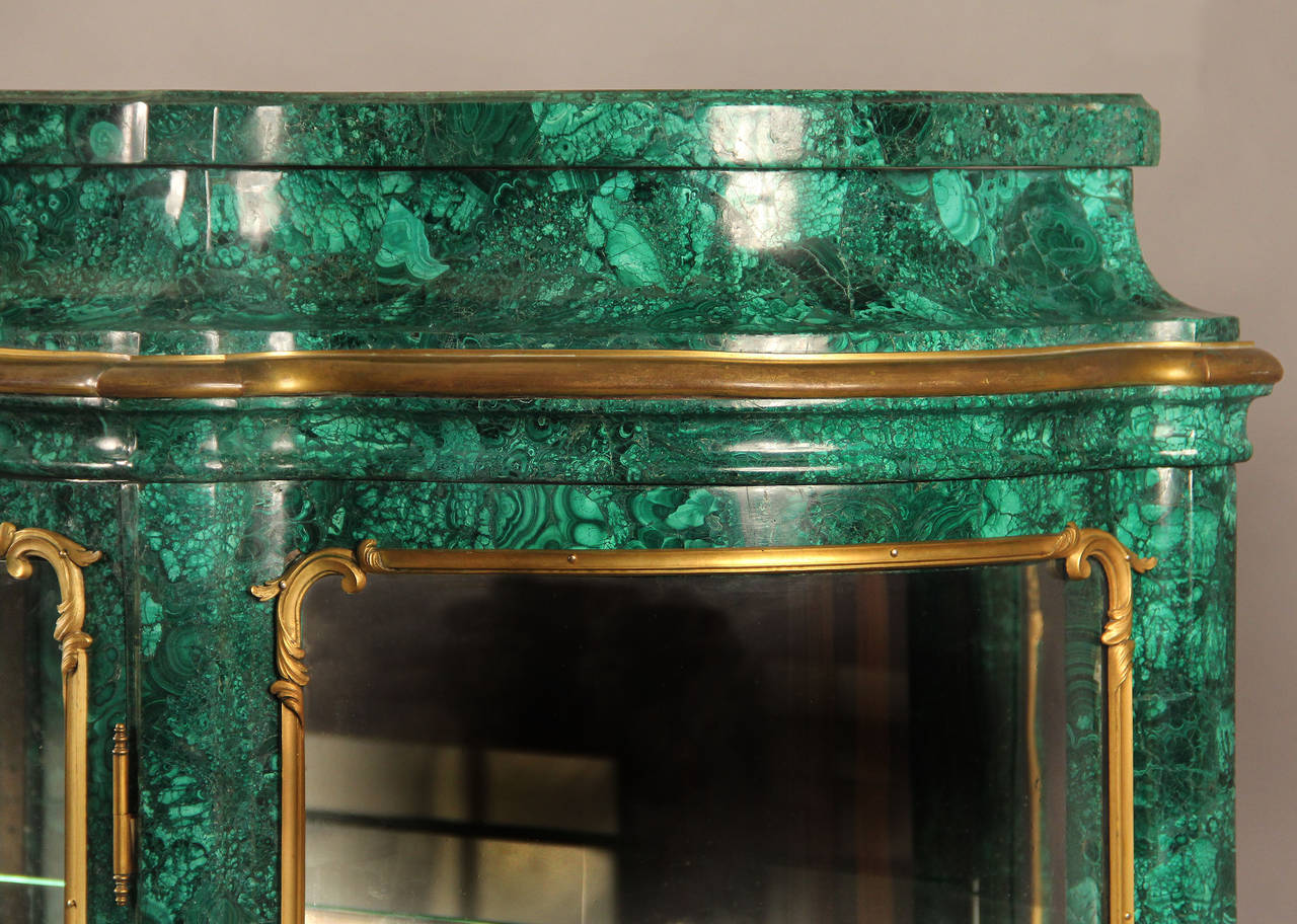 A beautiful late 19th century gilt bronze-mounted Louis XV style malachite vitrine.

A fine malachite top above center door with gilt bronze cornucopia and florals, bombe glass sides with three shelves.

Malachite is a semi-precious stone and