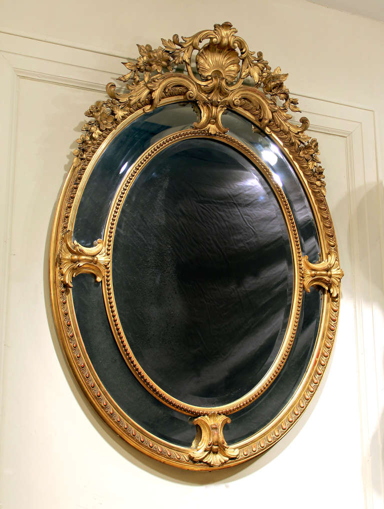 A stunning late 19th century carved giltwood and gesso mirror.

Of oval form with sea shells and flowers along the top. The glass is triple beveled with a center and four outside mirrors.