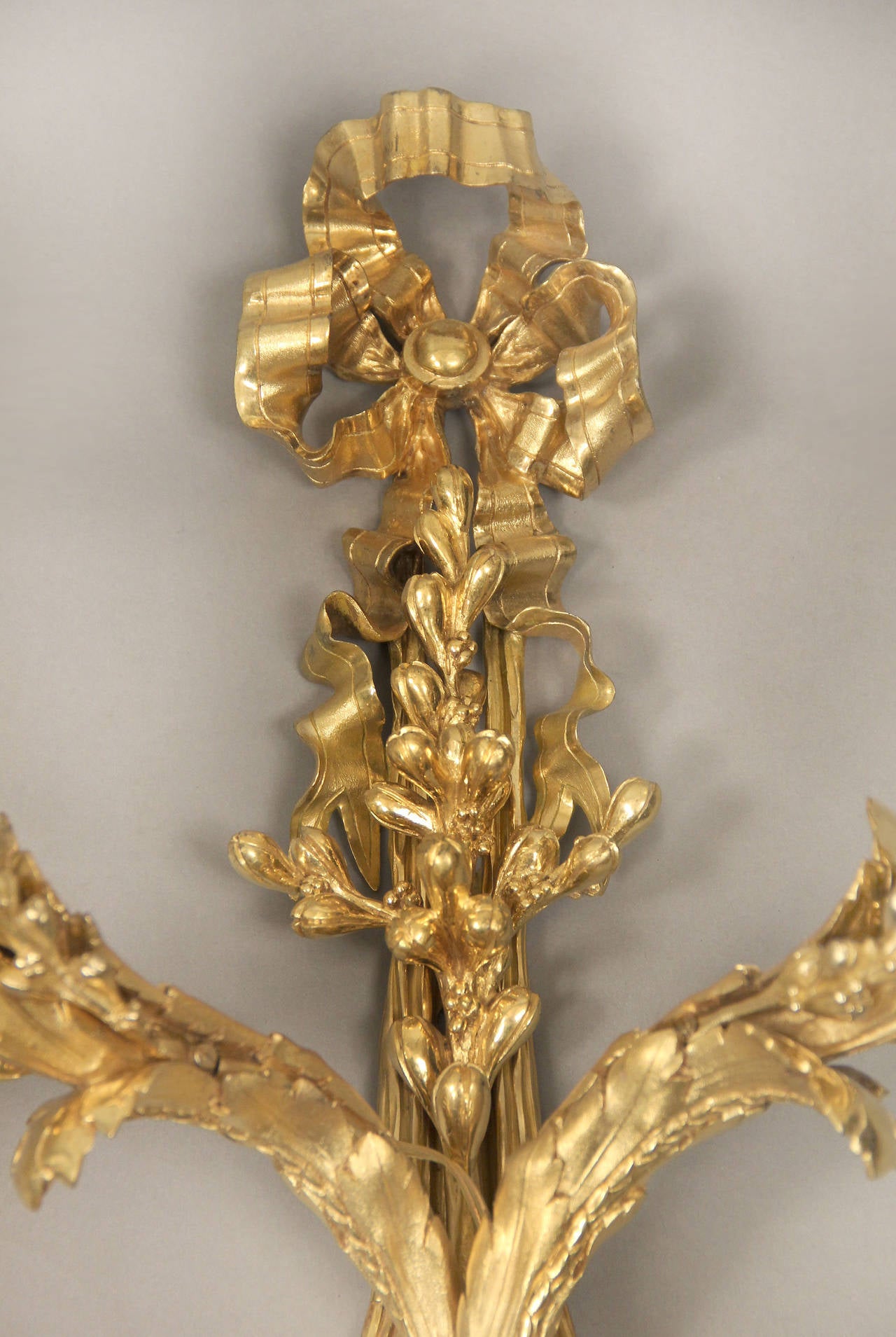 A wonderful set of four late 19th century gilt bronze two-light sconces.

Each with a ribbon tied support suspending two scrolling foliate branches.

 