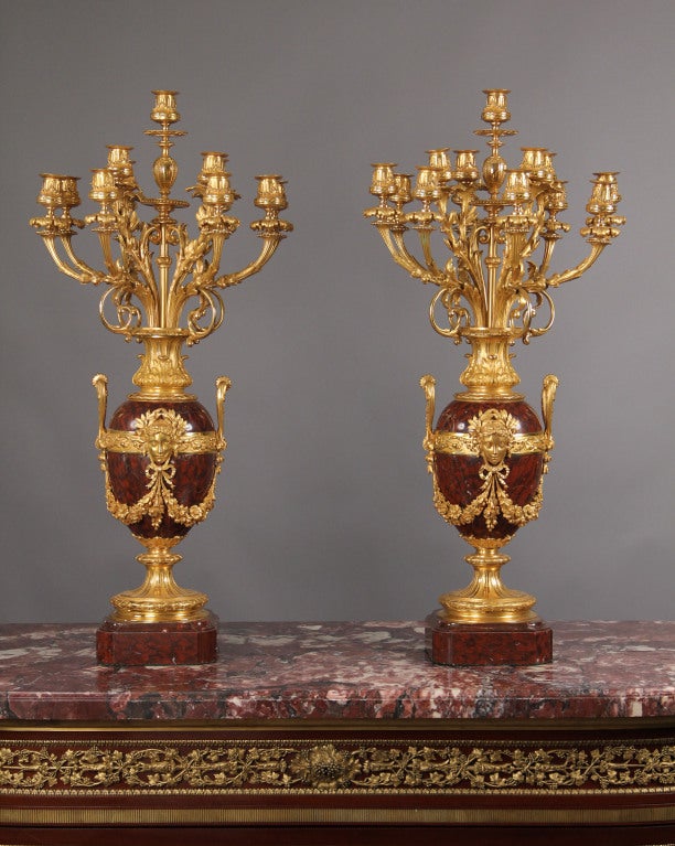 Opulent pair of late 19th century French 13-light candelabra.

Composed of gilded bronze and Rouge Royale marble in the Louis XVI taste, the two-handled vases richly mounted with female masks and floral garlands, the pair supported on thick square