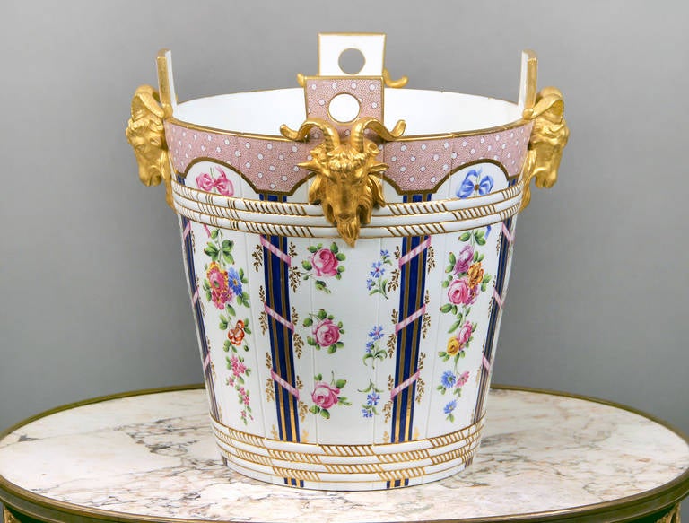 A beautiful late 19th century Sevres style porcelain parcel-gilt milk pail.

Modeled after the Tinette de la Laiterie de Marie-Antoinette a Rambouillet, with four gilt ram's heads and painted with loose bouqets within ribbon-tied reed bands.

