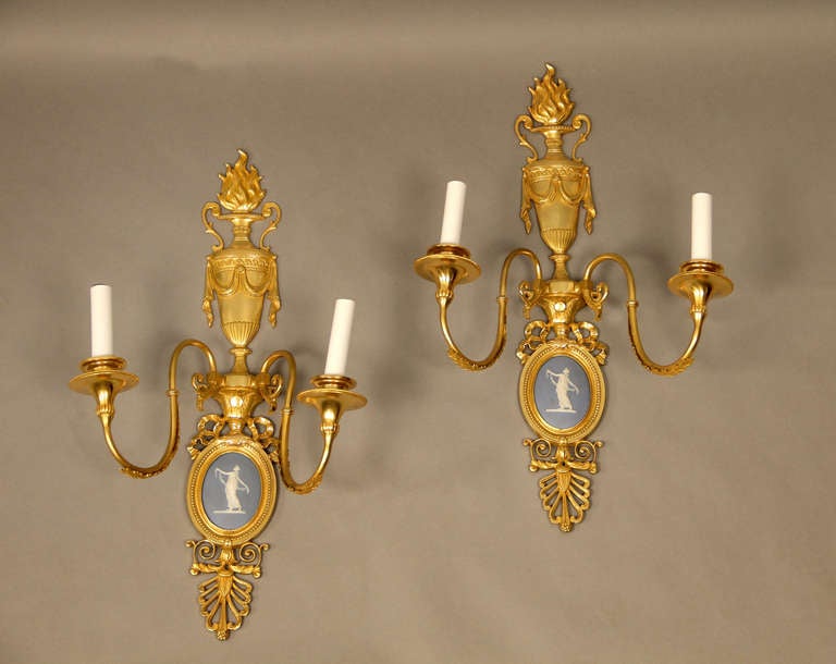 Pair of late 19th century Louis XVI style gilt bronze and porcelain two-light sconces

Each backplate decorated with a Wedgwood plaque and a flame emanating from an urn.

 