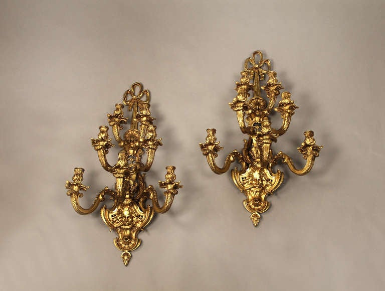Pair of late 19th century gilt bronze seven-light sconces.

Each backplate decorated with a bearded male mask, followed by three tiers of candle arms and ending with bow knotted ribbon.

 