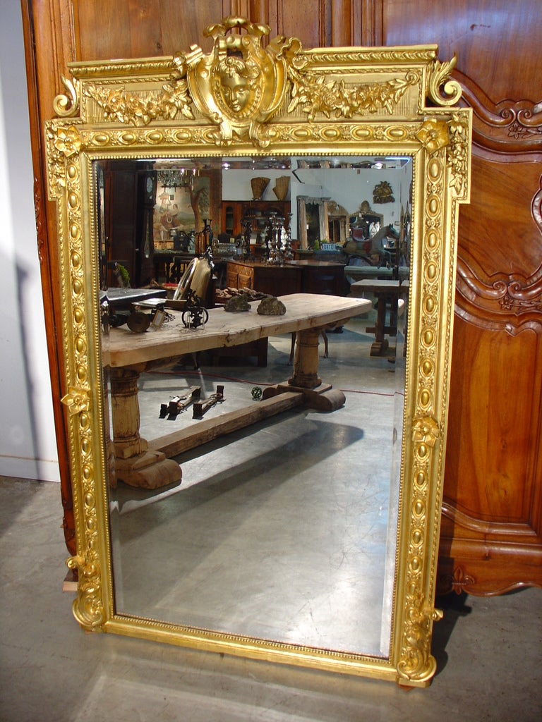 This stunning antique French giltwood framed mirror will be an elegant addition to any area it is placed in.  Its lines are geometric while its motifs are typical of the Louis XVI style.  There are cabochons, foliate and floral motifs, a central