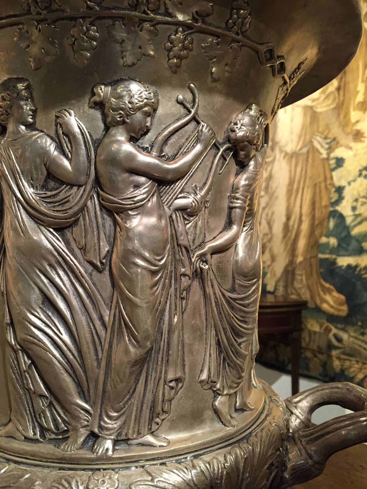 This pair of urns is cast from from metal (possibly brass), and then silvered for a beautiful finish.  They most likely date to the early to mid 1900's, and each one is decorated with Grecian or Greco-Roman motifs.  The main body has a surround of