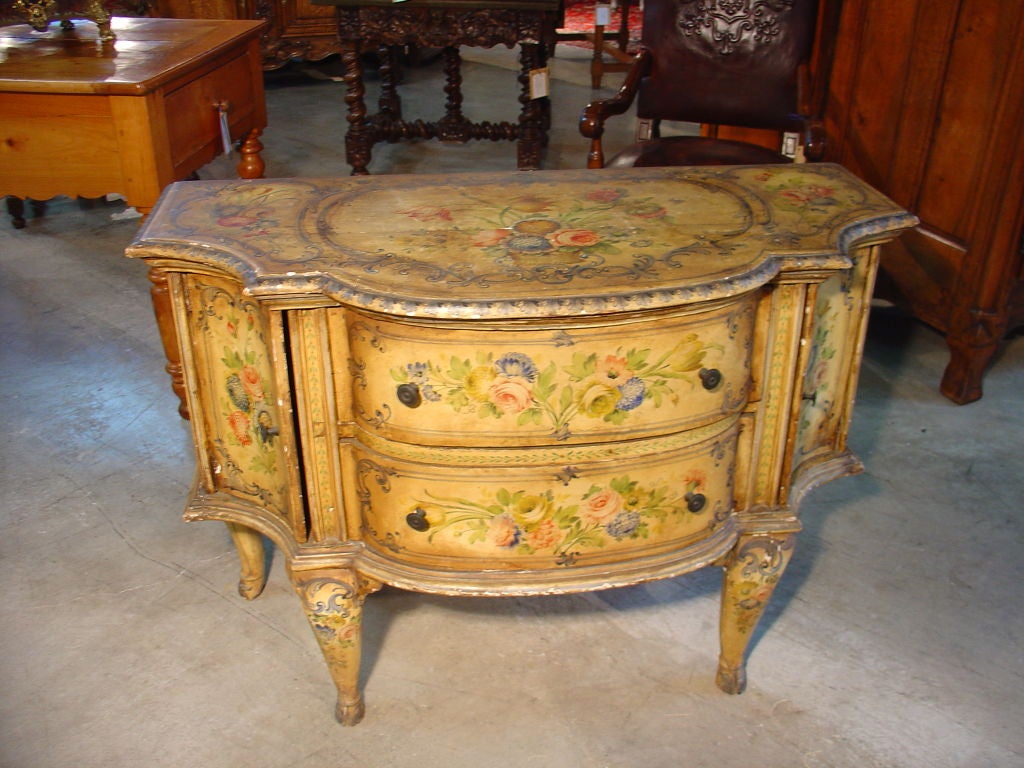 This painted antique Venetian 2-drawer, 2 door commode has painted floral bouquets surrounded by c and s-scroll leaf  borders. The overall color is the much sought after muted yellow ochre with pale and medium blues, greens, and roses. There are 2