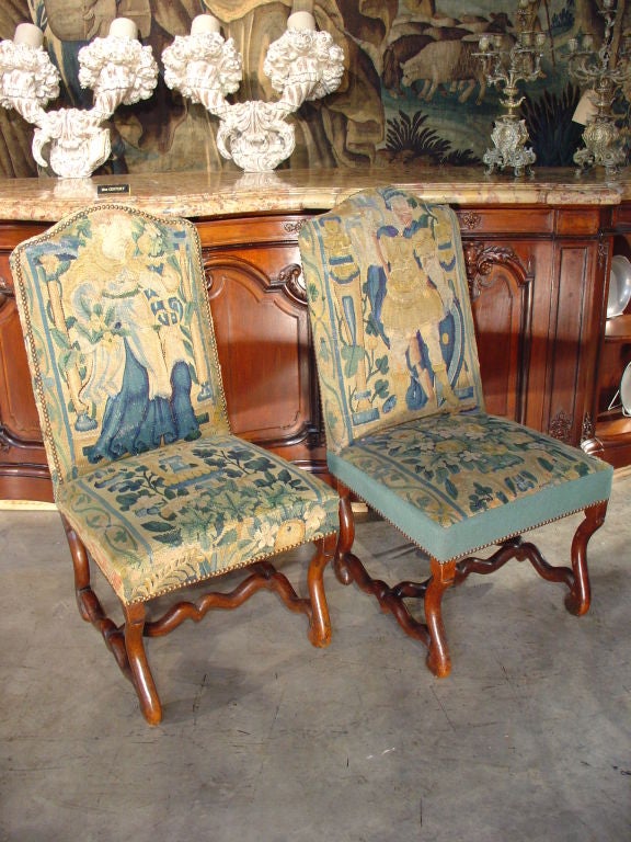 An Antique Pair of French Louis XIV Mutton Bone Chairs with Upholstery of 18th C. Tapestry Fragments  (due to the upholstery being made from fragments, details are dissimilar. One chair has a skirt border  while the other does not.  In our opinion, 