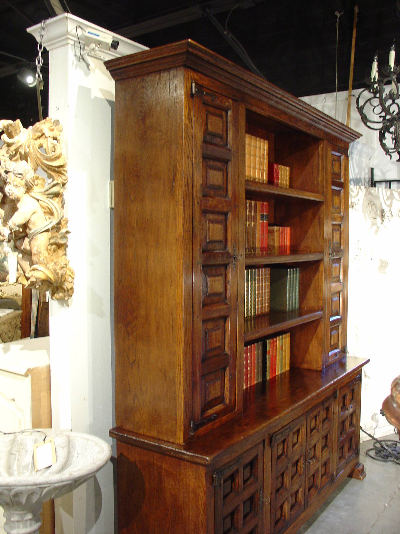 This elegant and well built two piece bookcase from Spain has raised beveled motifs on its front panels, with shaped iron hinges on the doors.  The upper indented cabinet has an open area with three shelves flanked by two bookcases with doors and