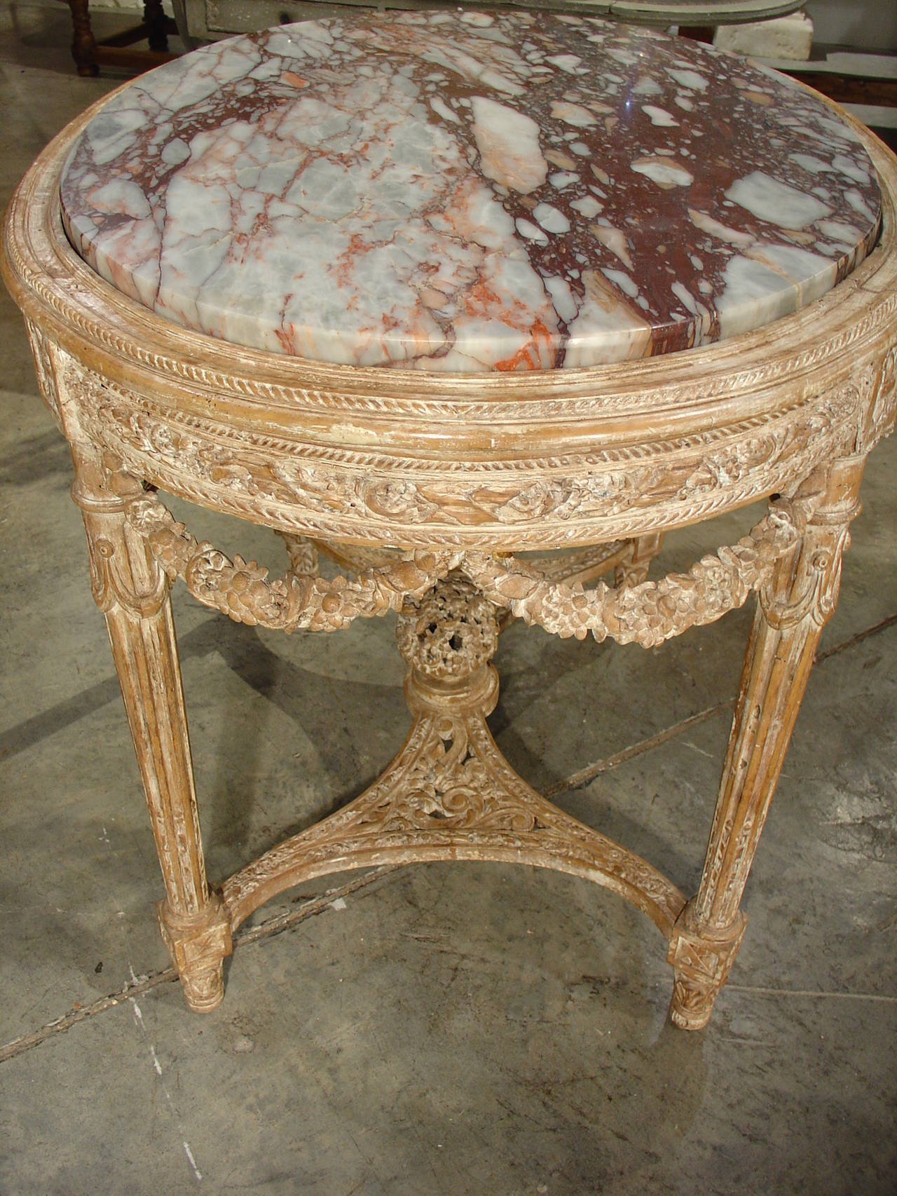 Beautiful up close as well as from a distance, this elegant parcel paint, antique French, Louis XVI style center table is the epitome of ornamentation in the Louis XVI period. The hand carving of flowers, ribbons and garlands on the table is packed