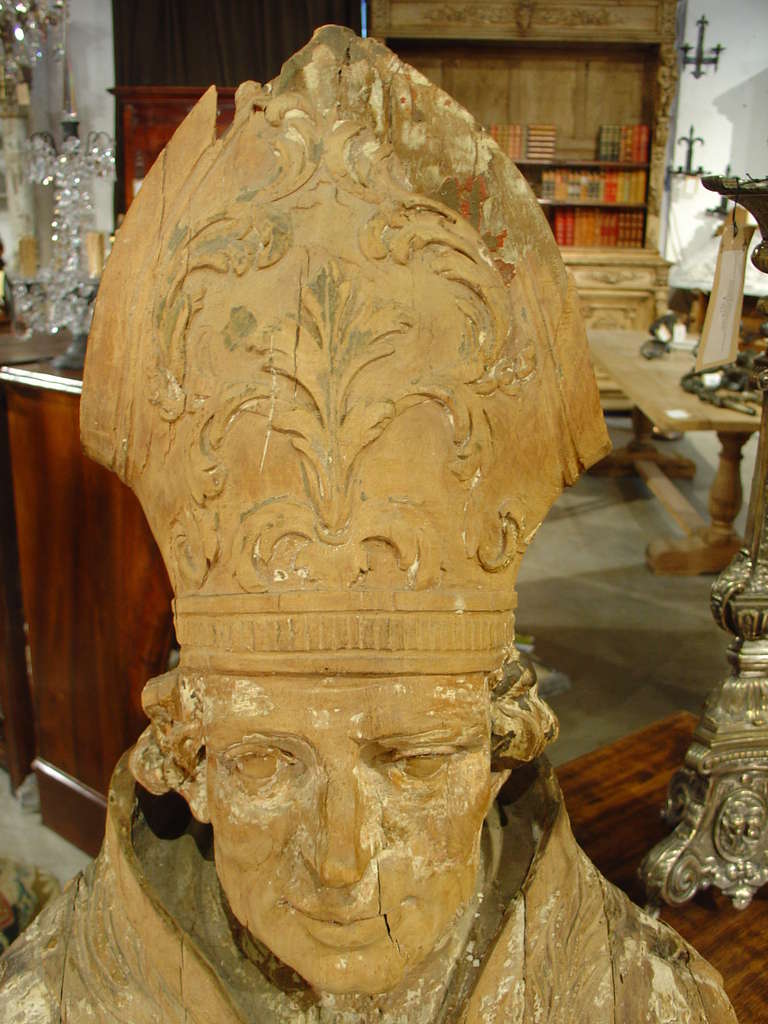 This French,  17th Century polychromed bust of a Bishop has been magnificently hand carved from one piece of wood.  His vestments have motifs of husks, various foliate motifs, a cartouche of acanthus leaves with a stylized fleur de lis at the