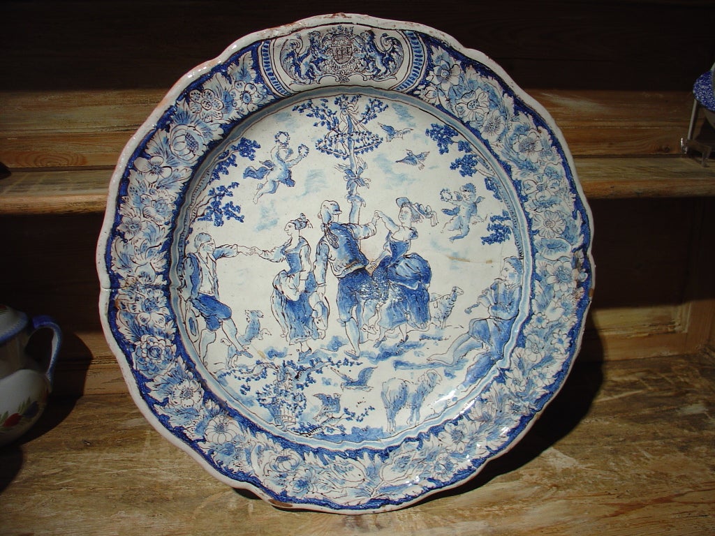 This rare 18th C. large faience plate from Nevers has colors of blue and white with lines of black or charcoal outlining the details.  The painted scene depicts a festive outdoor gathering with people dancing and musicians playing. There are lambs,