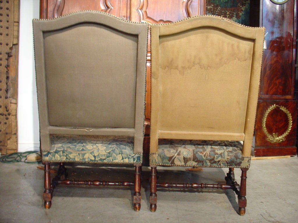 These magnificent antique French armchairs were hand carved from walnut wood in the 1800’s.  They have been upholstered with Aubusson tapestry fragments woven in the 1700’s. The arms curve downward and end in stylized dolphin heads that rest upon