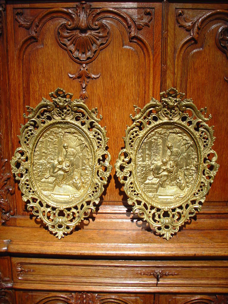 This pair of antique French cast bronze bas relief plaques depicts two people in a garden setting.  One is seated upon a vine covered stone bench painting pottery, while the other appears to be critiquing the work.  There are various other pieces of
