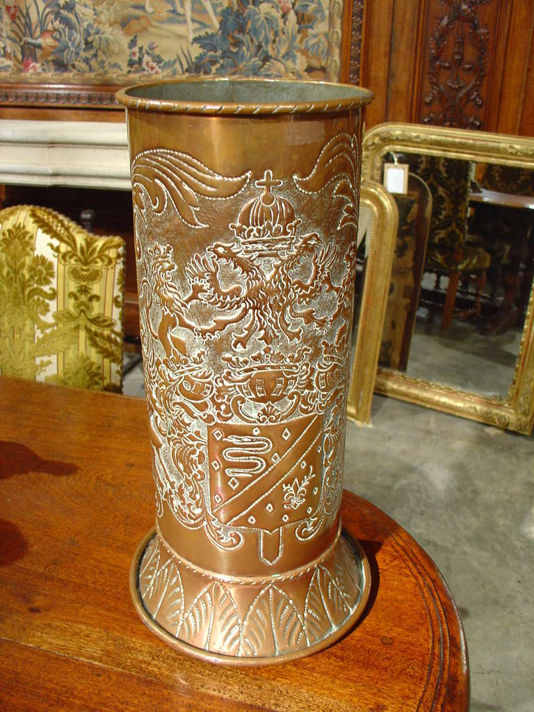 This charming antique French copper umbrella holder has fabulous hand punched and repousse motifs depicting a coat of arms on one side and the Fleur de lis surrounded by scrolling acanthus leaves. The curved base features stiff leaf motifs. Note the