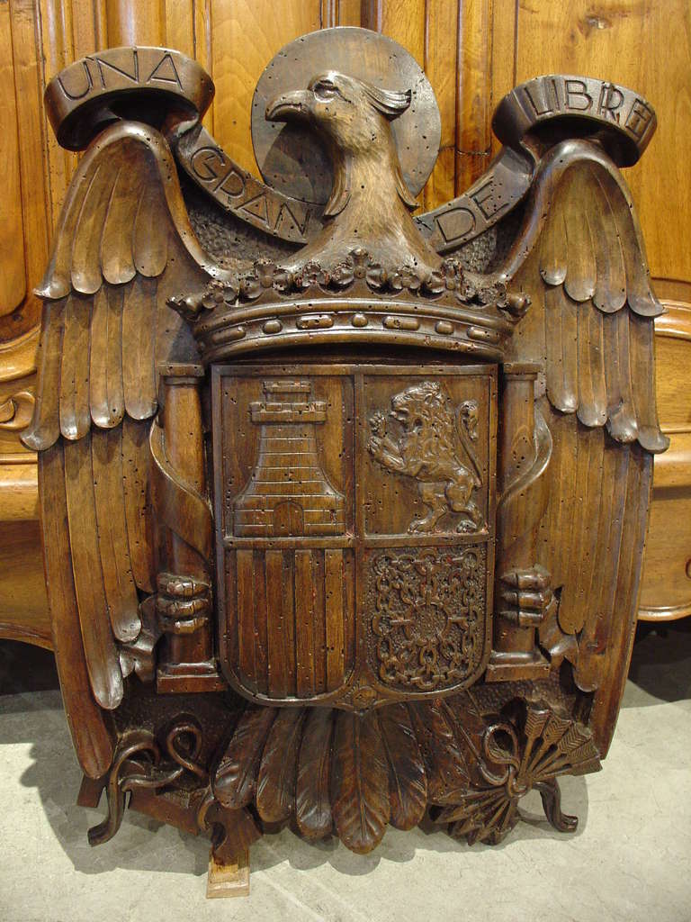 This plaque has been carved out of walnut wood, and it is a representation of the Spanish coat of arms. It most closely resembles the armorial representations starting in 1938 because we see the words UNA GRANDE LIBRE. This was the motto of Spains