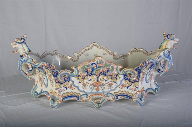 This large and beautiful Desvres faience jardiniere is in the Rouen style of decoration.  The colors are royal blue, pale blue, yellow, orange sage green, pale green, and taupe painted on a glistening white ground.  There are two half-figures at