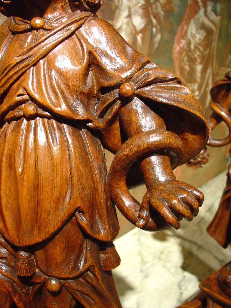 This is rare and stunning pair of hand carved wooden statues holding cornucopias, which also serve  as candlestick holders .They are from Flandres and date to the 1600’s. They stand on bases which feature a frontal cartouche of cherubs’ heads at the