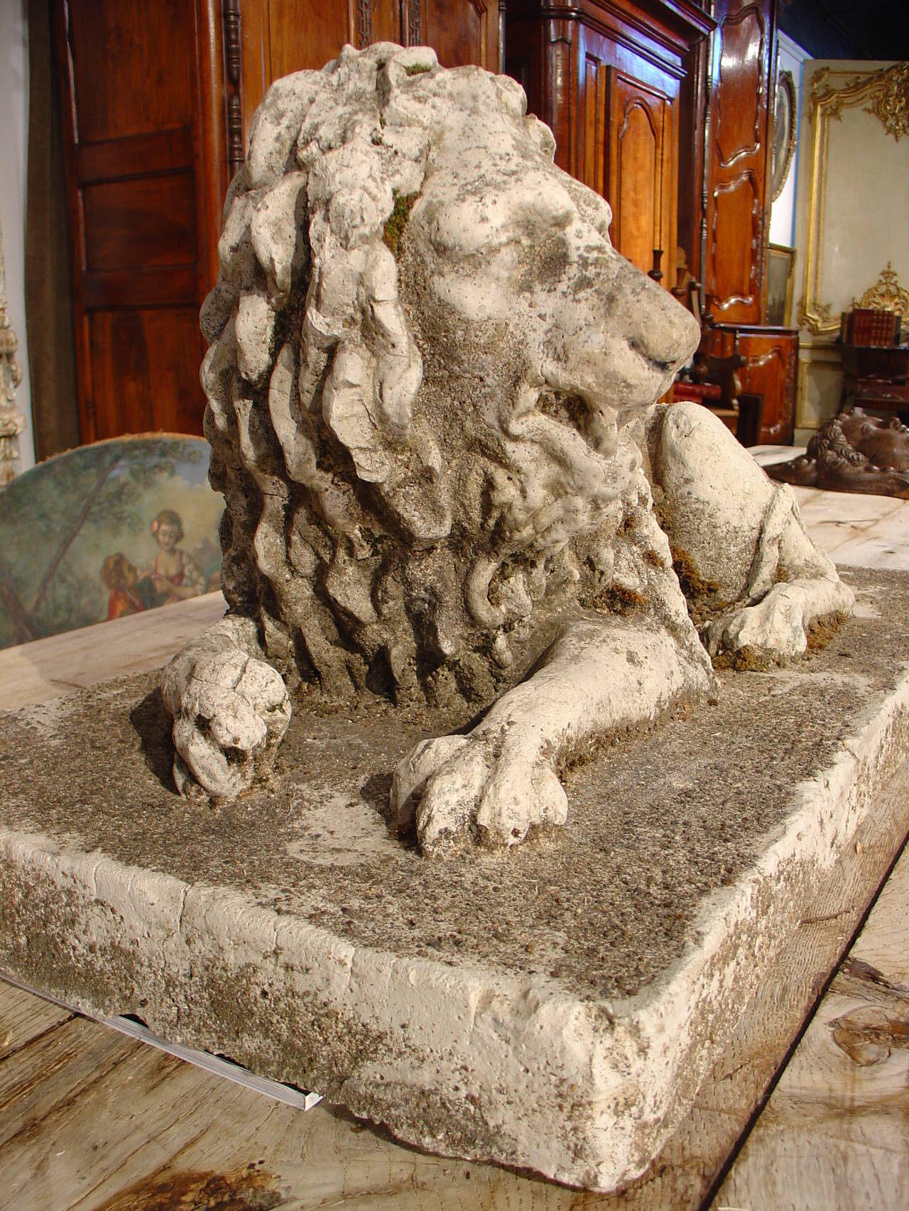 This is a 19th century French reconstituted stone lion statue lying down on a rectangular base. The sculptor who did the original of this statue has portrayed the lion in a reclining position on his right side. His right paw is curled inward and his