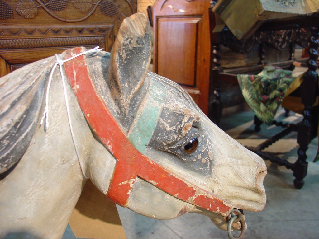 This delightful and charming children’s French carousel horse has a red seat with a back instead of a saddle.  The horse is white with grey markings around the eyes, ears, mane, legs, feet and tail.  The seat and bridle are red as is the saddle flap