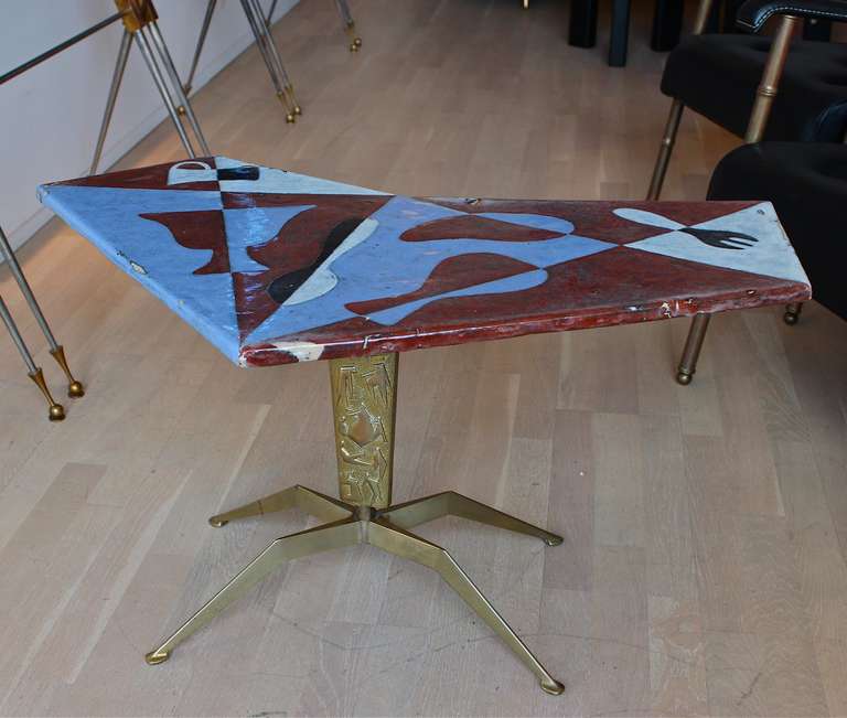 Table with cast brass base and ceramic top. The delta shaped ceramic top sits on its brass base which is cast with abstract figures and ends on an angular brass foot.