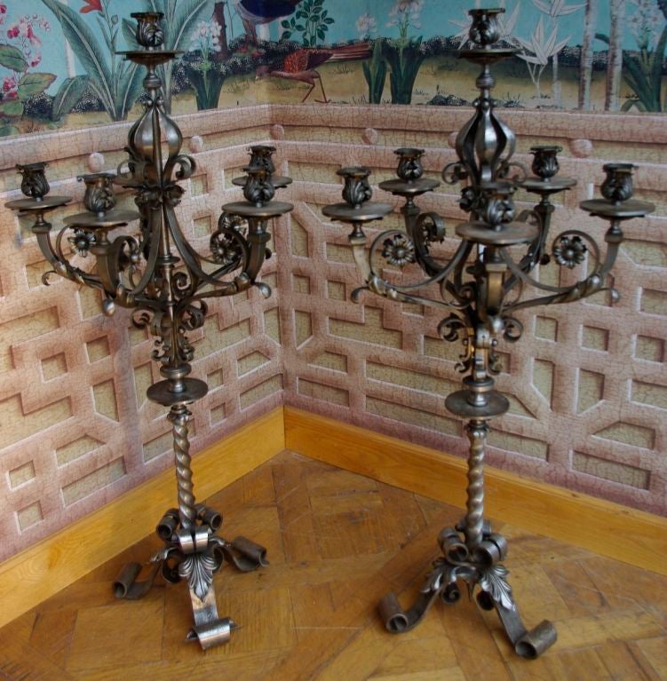 Pair of Medieval style wrought iron candelabra, standing on three scrolled legs topped by acanthus leaves.
The twisted central part supports six lights, five around the central part and one on the top. The lights are decorated with volutes and