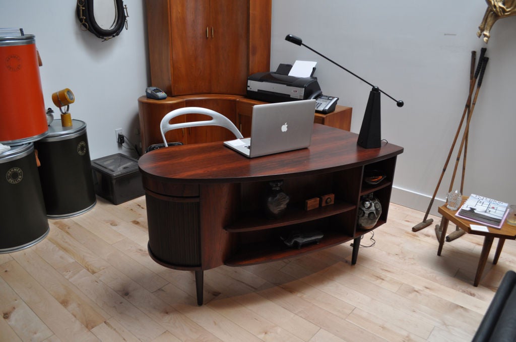 Danish Modern kidney shaped desk. Beautiful Midcentury Modern Piece. Rosewood desk with revolving mirrored bar, and seperate utilities sorter (rotating) above. Drawers to left side and shelving on front.