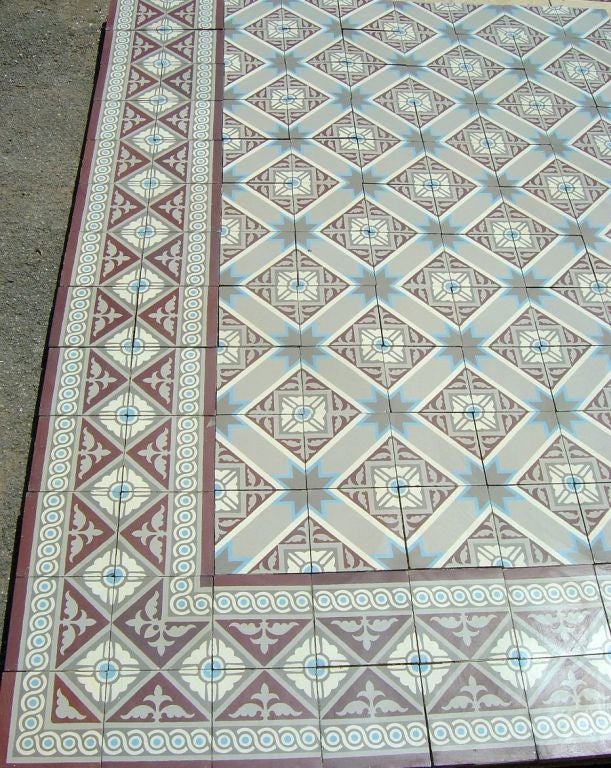 A small and complete ceramic encaustic entranceway floor, totaling 75 sq ft, dated 1920. The floor consists of a principal field tile in off white and grey with a starred blue motif, complimented by an ornate double back to back border tile in
