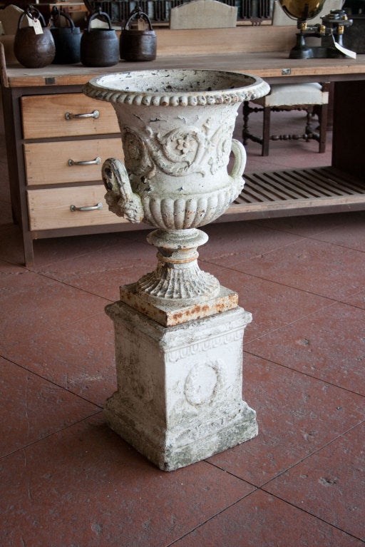 A beautiful Victorian cast iron half-fluted campana garden urn. It has a gadrooned rim above a deep cast frieze with leafy scrolls and loop handles to sides that are cast with masks. It sits atop an associated composite base with laurel leaf