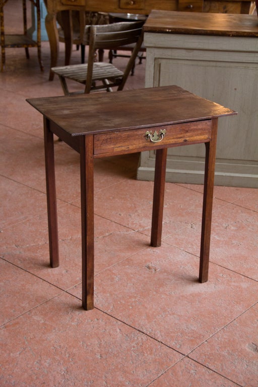 A simple basic late 1700s mahogany English side table of the George III period. The 4 simple legs are chamfered. The drawer pull is a later addition.