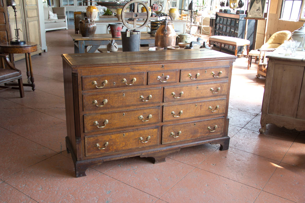 Late 1700s English Georgian oak linen chest on stile feet. The two top rows of drawers are blind and the bottom two rows pull-out. The top lifts to store blankets. The brass hardware is original or bar one replacement.