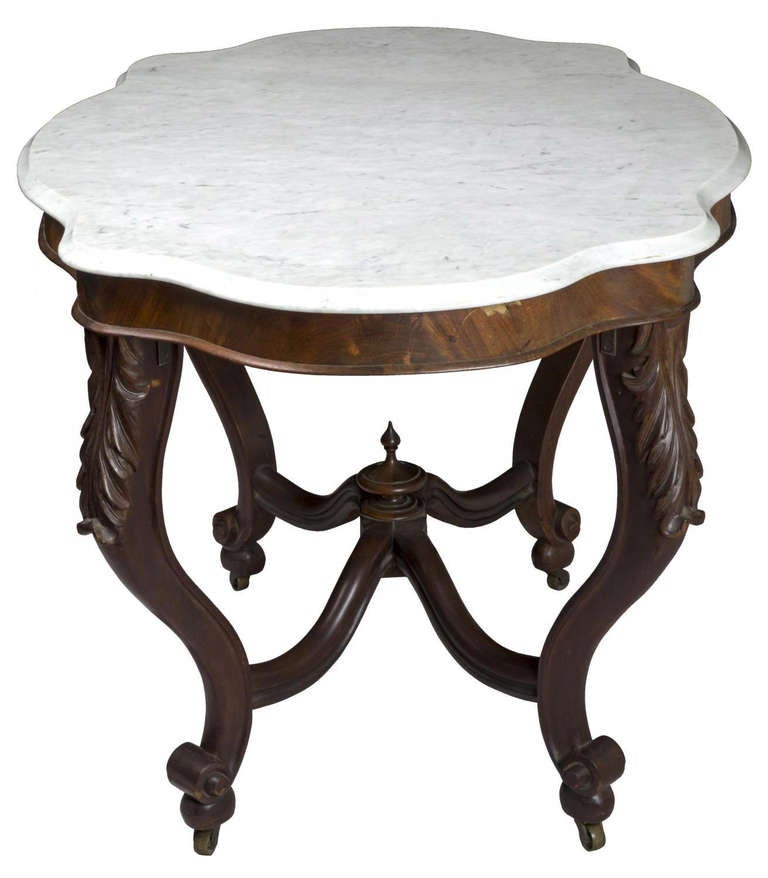 Retaining its original shaped marble top above a crotch grain mahogany apron, this table is supported on four French cabriole legs embellished with exuberantly carved acanthus carving at the top of each leg, which terminate with a traditional Rococo