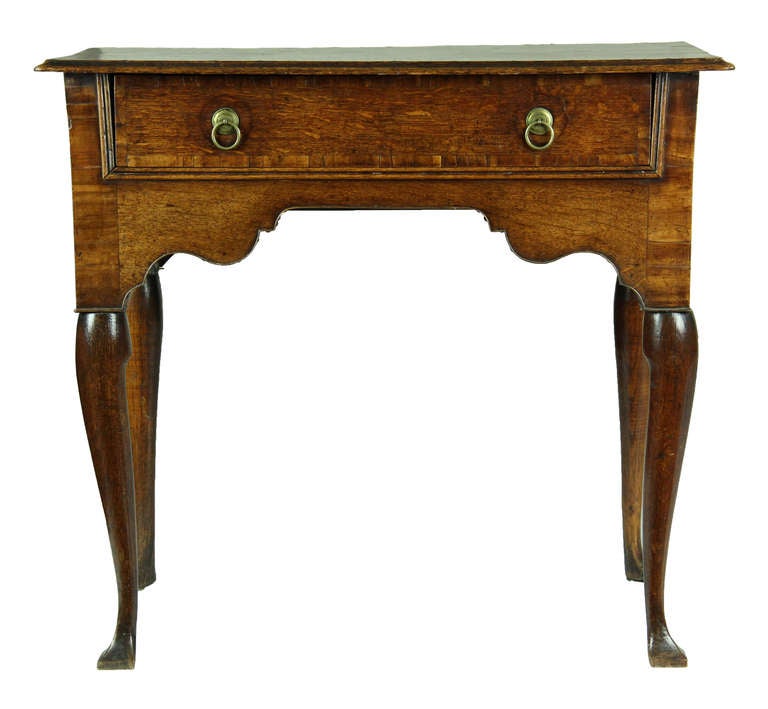 This one-drawer table has an elegant Classic Queen Anne shaped apron, all supported on cabriole feet. The top is of quartered oak and crossbanded with a light exotic wood, as is the drawer front. Tables such as these are used as side tables for