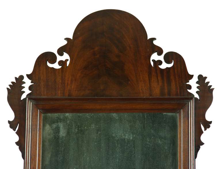 This is a good sized Queen Anne mirror composed of magnificent figured mahogany that has mellowed through the years. The glass, backboard, etc. are all original and the Silhouette carving of this mirror is extremely well developed and one of the