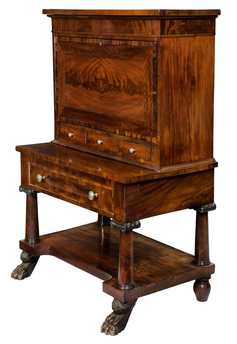 While this form can appear quite boxy and heavy in appearance, the use of four tapered columns, which are embellished with elegant carved scroll capitols, contributes to the openness of this secretaire. The carved paw feet also give height and are