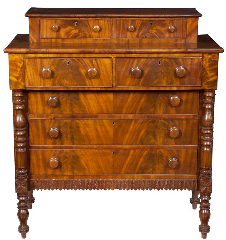 This bureau of highly figured mahogany has robustly turned columns and Sheraton style turned legs. It is notable in its exhibition of exuberant carving and detail, i.e. the carved apron and distinctive four-part leaf flanking the apron. This