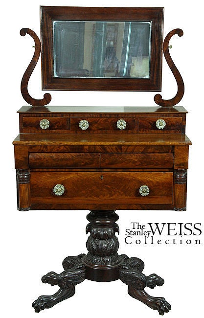 A rectangular mirror is supported by lyre scroll arms above three horizontal drawers and further developed with larger drawers below flanked by opposing columns. The upper case is supported by a well-developed carved column and carved paw feet with