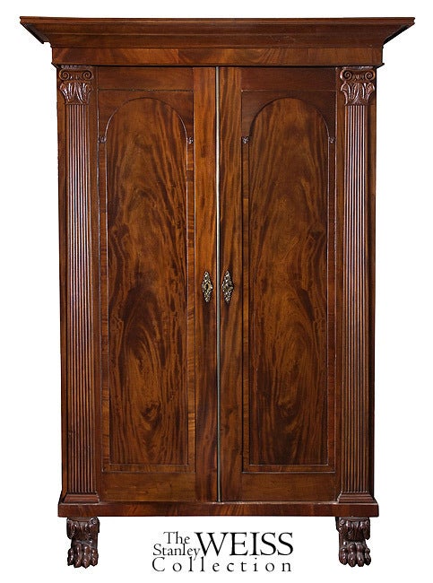 Strongly reeded columns flanking each door with detailed capitols below a strongly developed cornice top molding define this armoire. While this entire case piece is composed of solid mahogany, the doors are of large, ribbon grained, contrasting