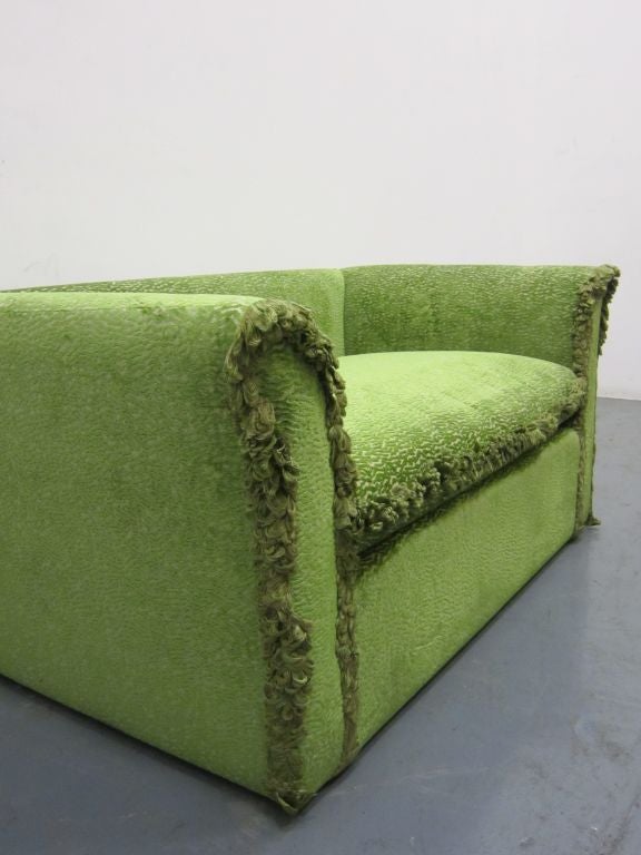 A highbacked two seater sofa in green upholstery and green fringing.