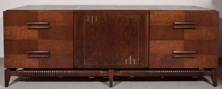 Mid century moderne cabinet or credenza in georgous woods and brass inlay. The whole sitting on beautiful carved apron and splayed legs. 4 drawers and 2 doors. Behind 2 doors are 4 more drawers. A superior quality piece made by Vanleigh, New York.
