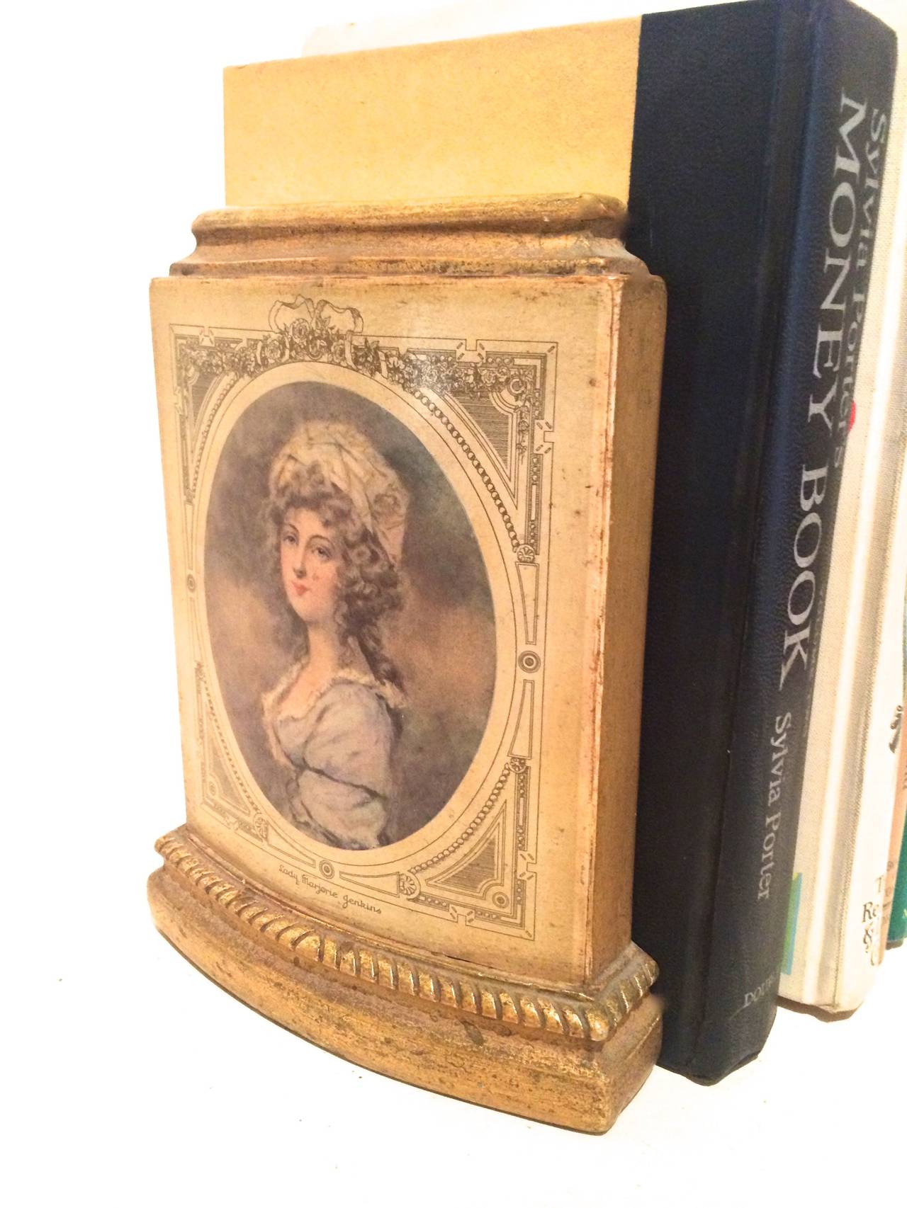 Pair of bookends depicting male and female period portraits. Gold and beige from Classic Italian designer, Borghese.

Metal stand rests flat between the two to hold books well this distance is 6