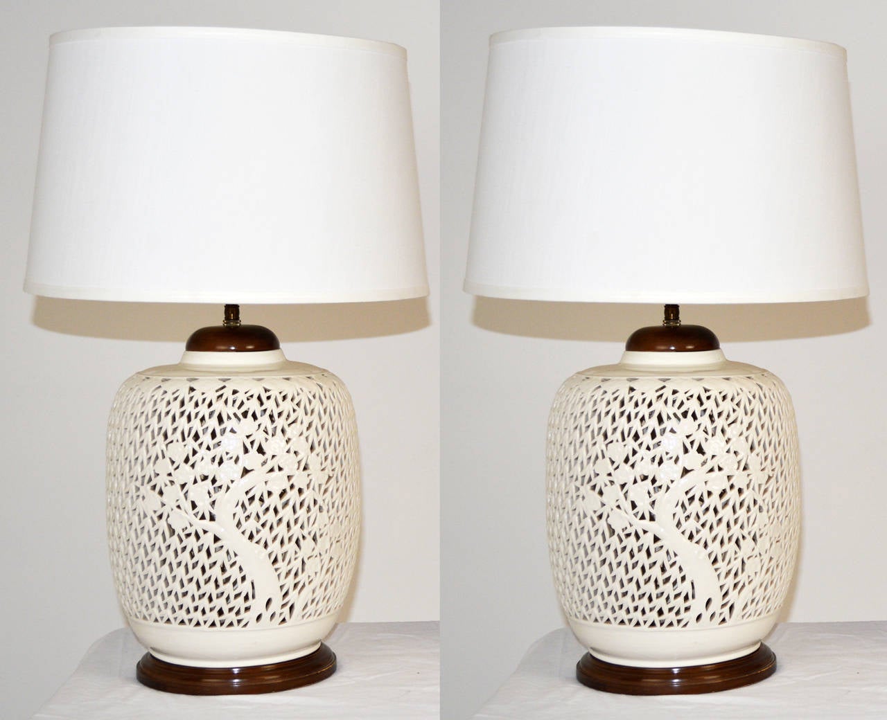 A beautiful pair of Chinese style reticulated porcelain Blanc de Chine table lamps with cherry tree motif. Stained wood base and CAP. Double socket clusters, 24'' to top of shade support. Shades not included, for display only.