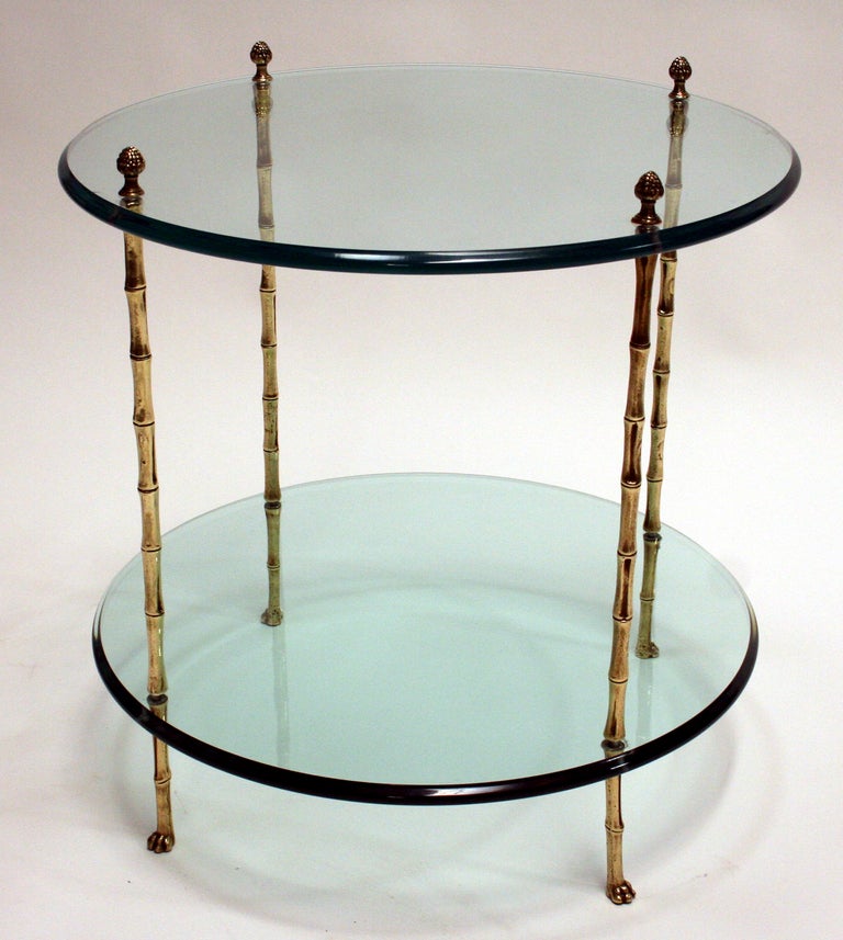 A lovely side table in the manner of Maison Jansen consisting of four faux bamboo brass legs with acorn finials and brass claw feet, supporting two glass plateaus with shaped edges. 