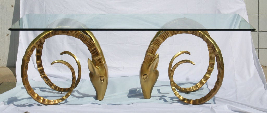 A pair of large Ibex heads with curling horns as the base for a glass top dining table. Bases are a patinated gold finish. Incredibly sculptural. Each base measurs 31