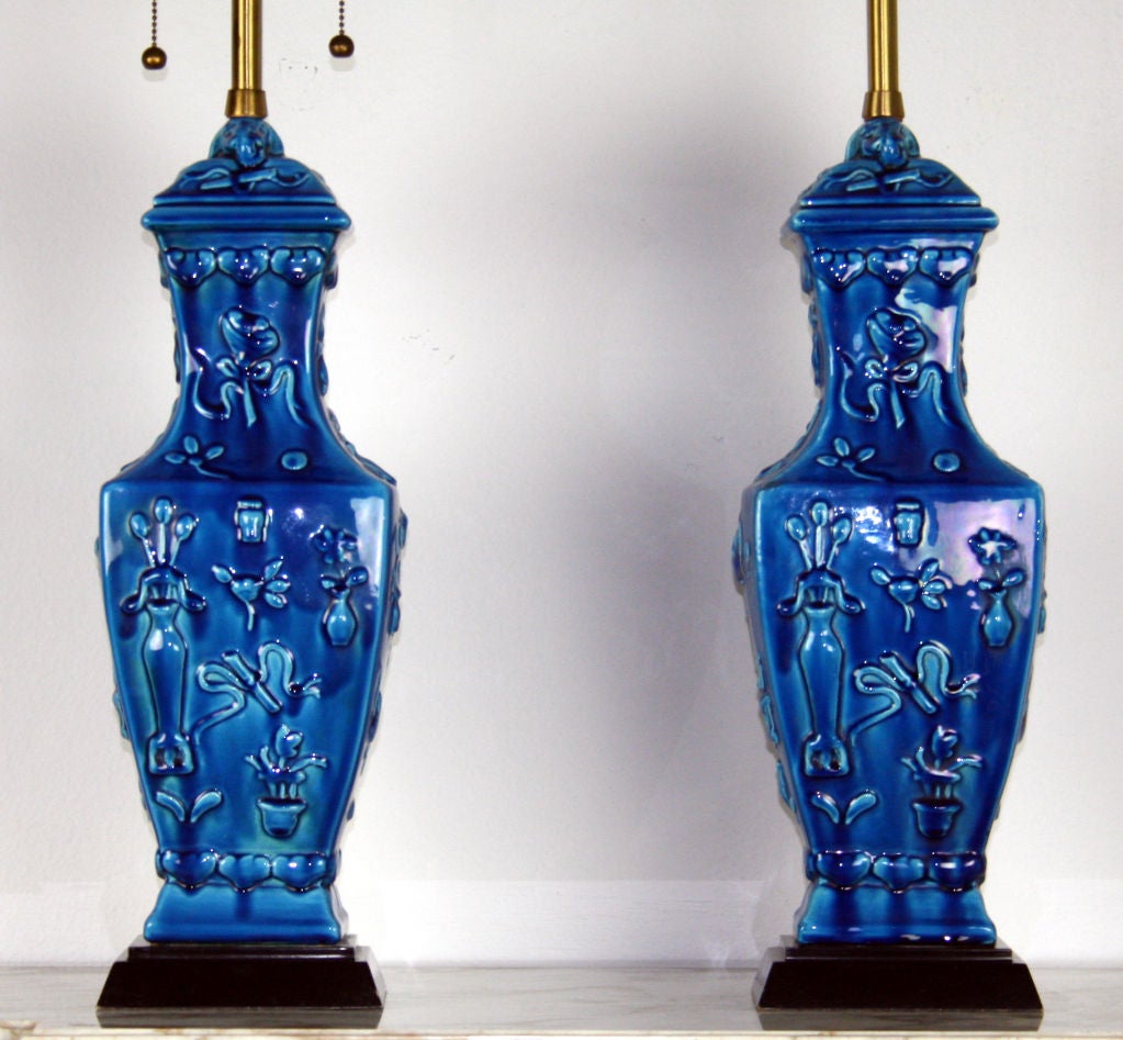 a pair of Marbro lamps. Beautifully glazed in a deep turquoise blue with marvelous mottling. Of rectangular baluster shape with floral decoration in deep relief. Double cluster brass sockets and black painted base. height of lamp body is 21.5