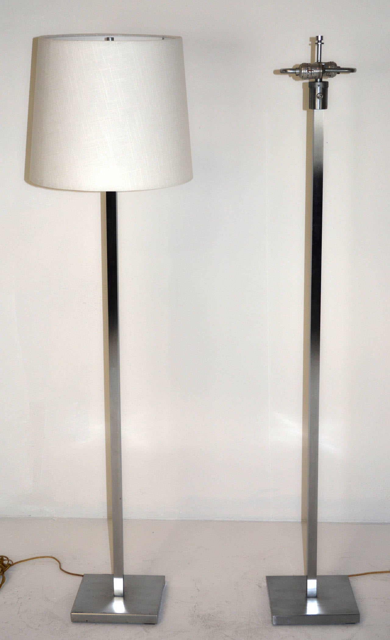 A pair of American floor lamps, mid-century, comprising a square aluminum shaft on a square base. Double sockets, with original finials. Shades for display only.