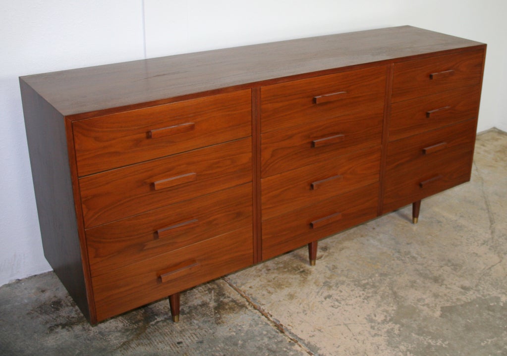 Elegant 12 drawer dresser in walnut with walnut handles. The case floats on three pairs of tapered legs with brass sabot.