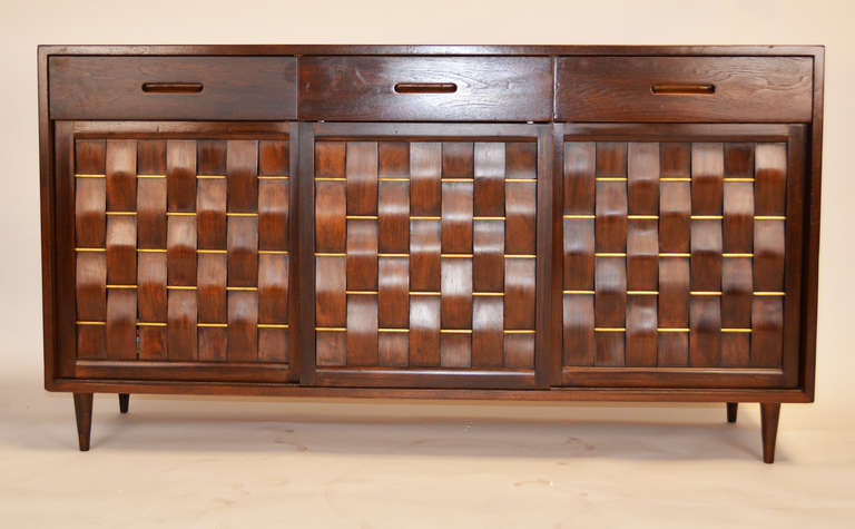 An excellent Edward Wormley for Dunbar woven front credenza. Mahogany construction with brass rods. Three sliding doors revealing adjustable shelf in the middle and on one side with a set of drawers on the other side. Three drawers above the doors