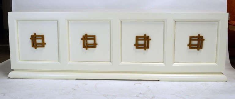 Sleek James Mont ivory lacquered four door cabinet with sculptural gilt wood handles. adjustable shelf in each compartment.