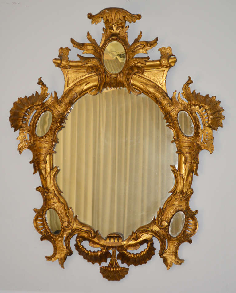 An oval mirror plate surmounted by rocaille mirrored cartouche cresting within an extravagant scrolling foliate carved frame containing a further five oval mirror plates. Possibly German or Italian. Projection at top is 6”. 