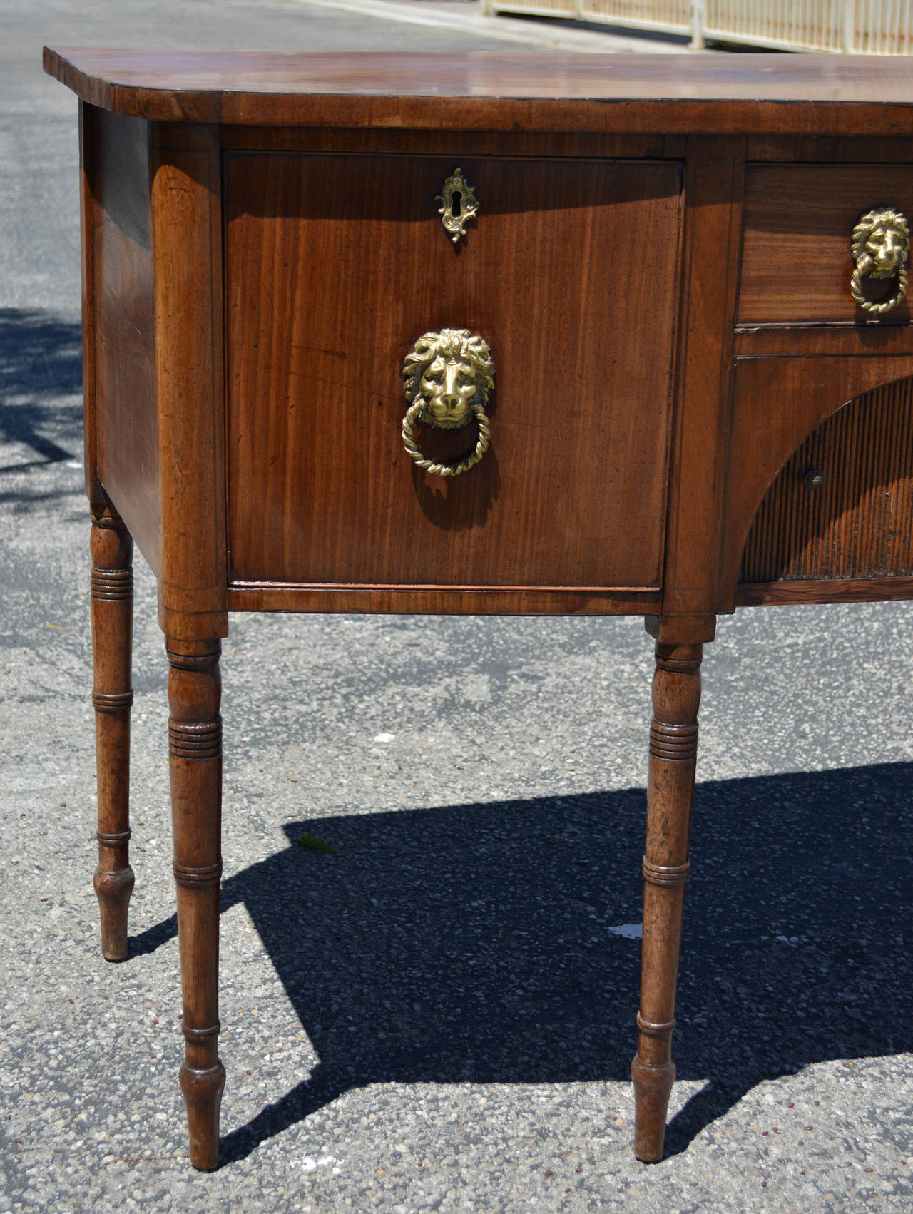 A lovely 19th century Regency bow front sideboard on turned legs with lion head brasses are with a central shallow drawer over a tambour door shelf, flanked by a deep drawer and cabinet. Good color and patina to the mahogany.